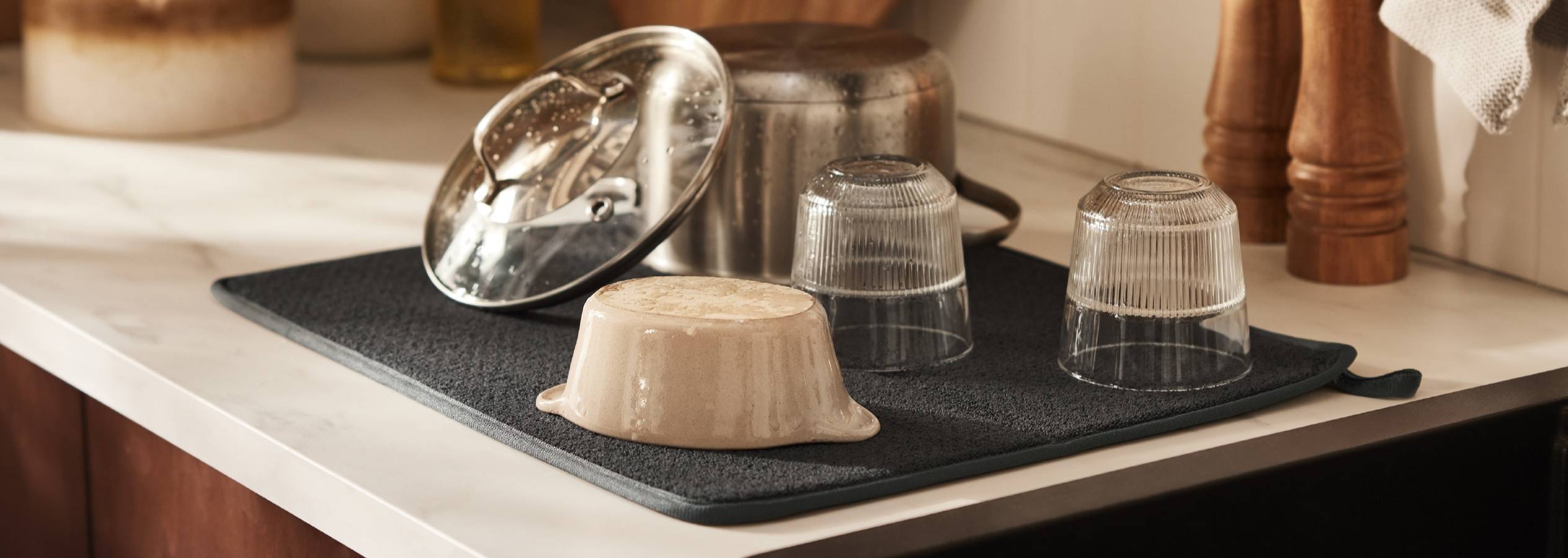 Et mørkegråt silikone underlag beskytter en marmor køkkenbordplade mod våde gryder, skåle og glas.