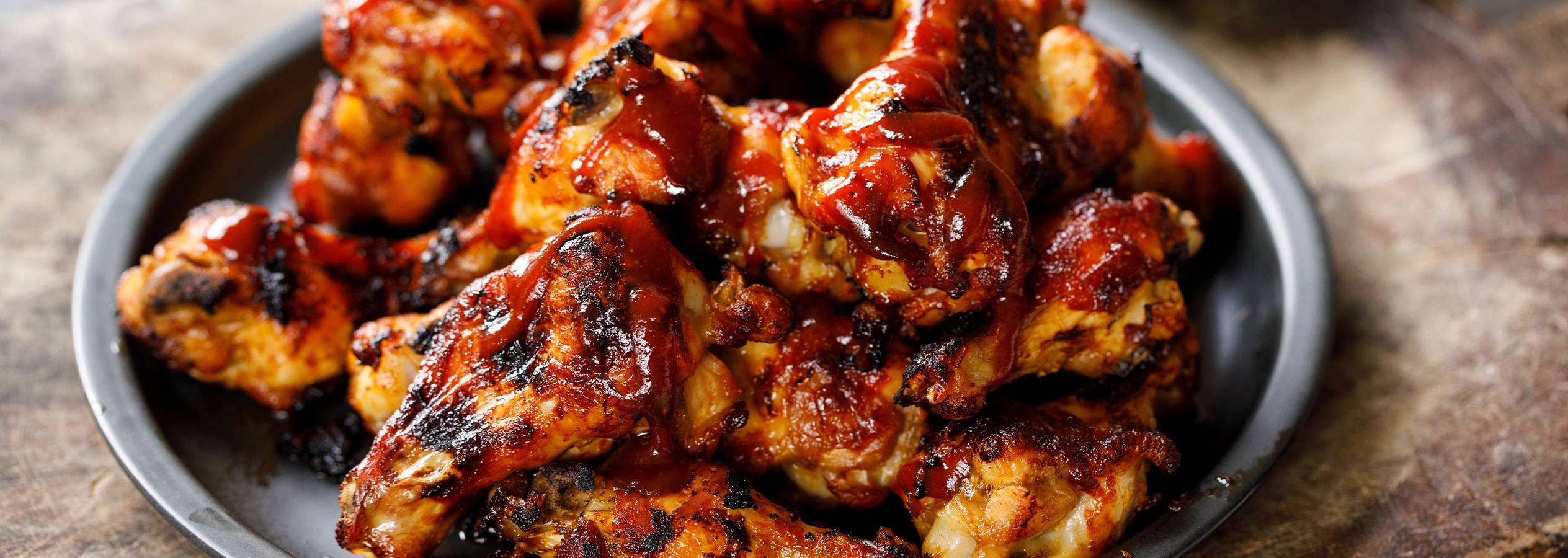 En mørk tallerken fyldt med lækre, grillede kyllingevinger i BBQ-sauce.