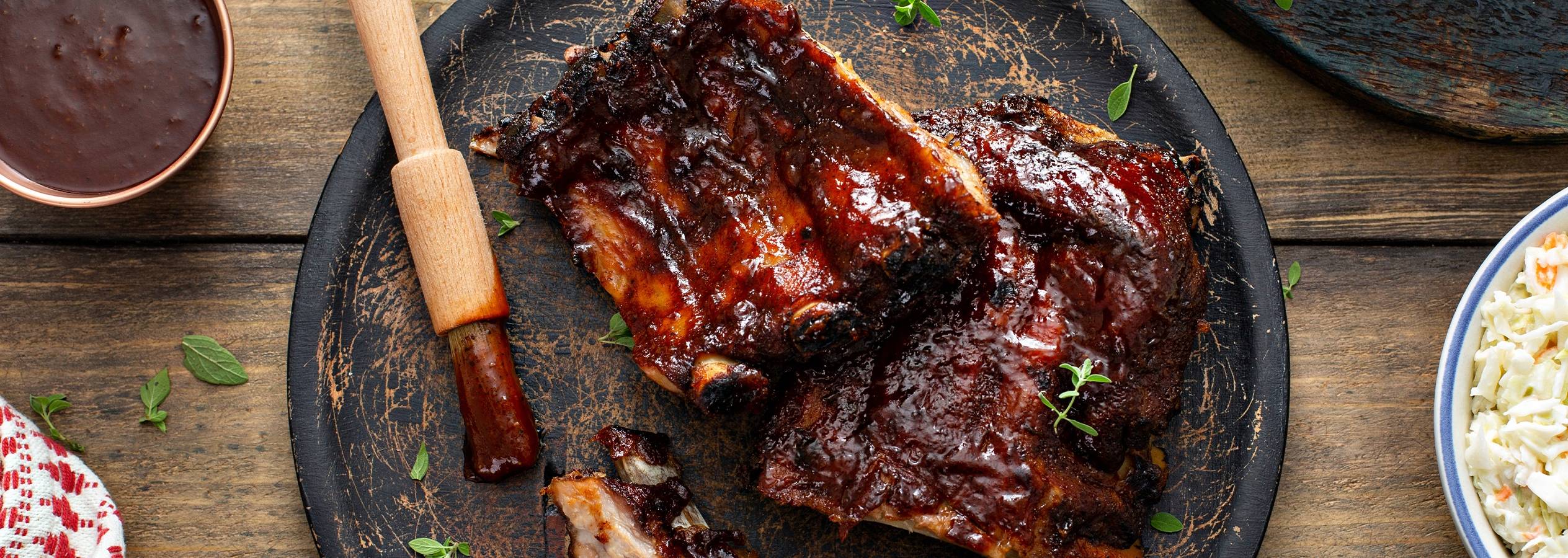 BBQ-ribbensteg serveret på en mørk tallerken med coleslaw og BBQ-sauce.
