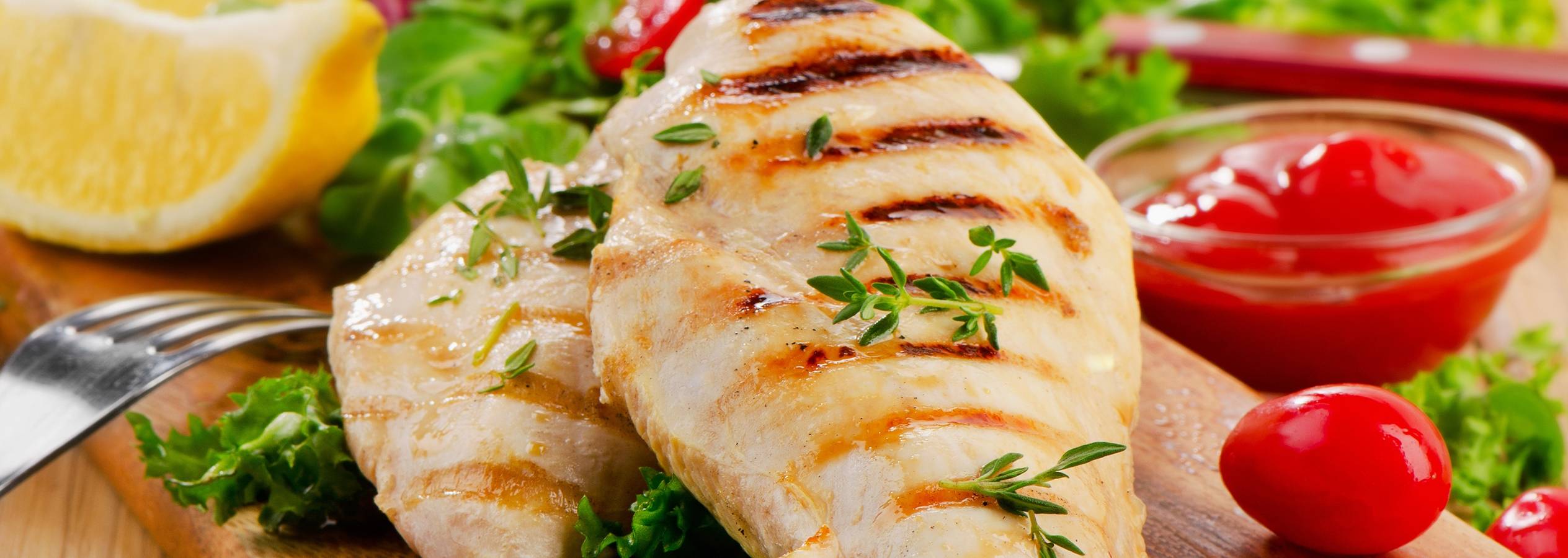 Grillerede kyllingebryster serveret med salat, citron og ketchup.