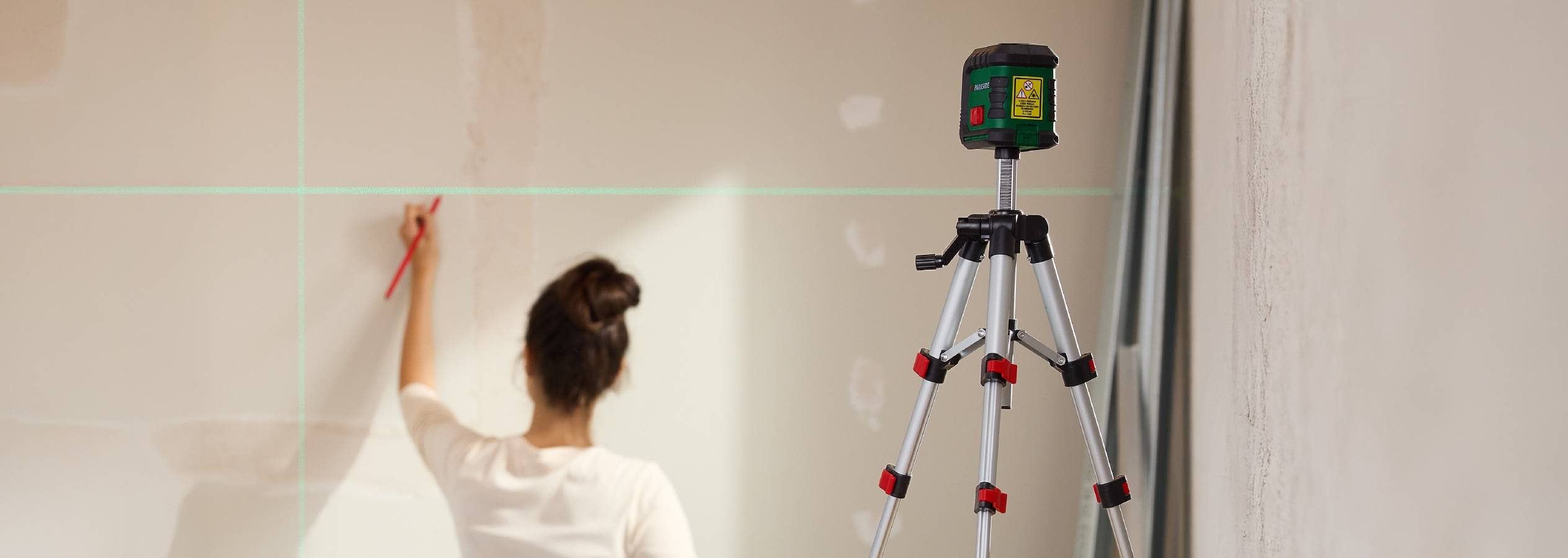 En kvinde bruger en laser til at markere en væg, med en laser på et stativ i forgrunden.