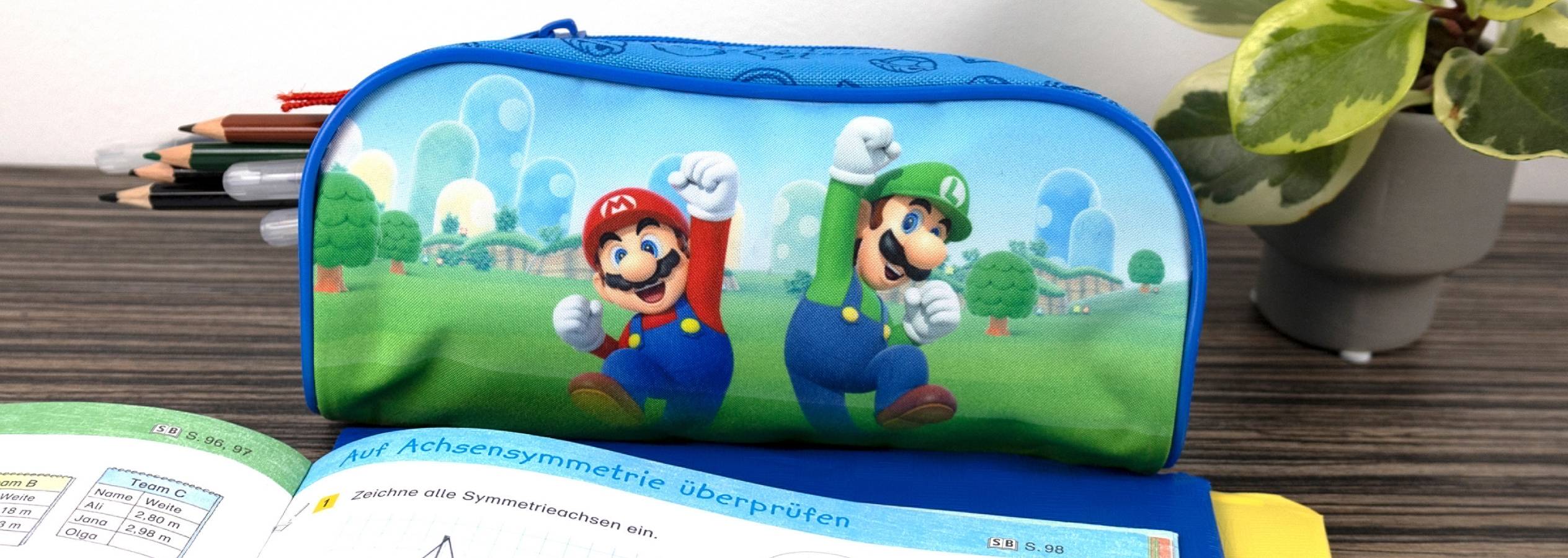 En blå penalhus med Mario og Luigi motiv ligger på et bord med skolebøger.
