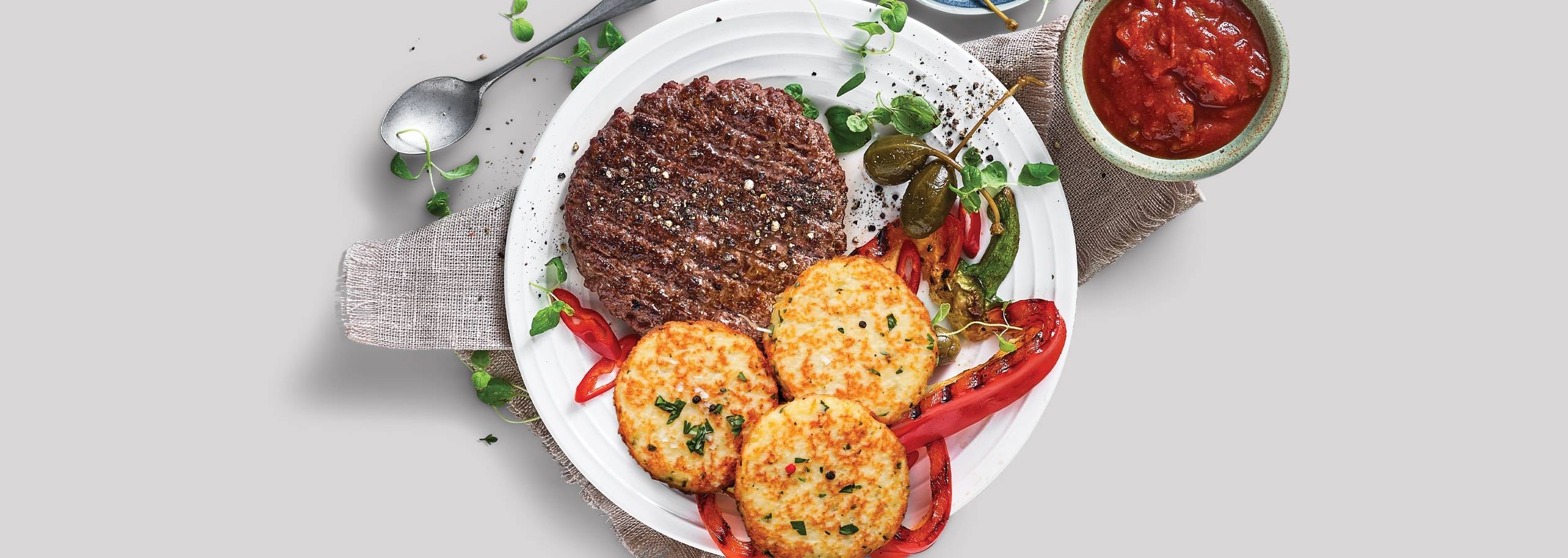 En saftig bøf serveres med sprøde kartoffelpandekager, grillede pebre og en lækker tomatsauce.