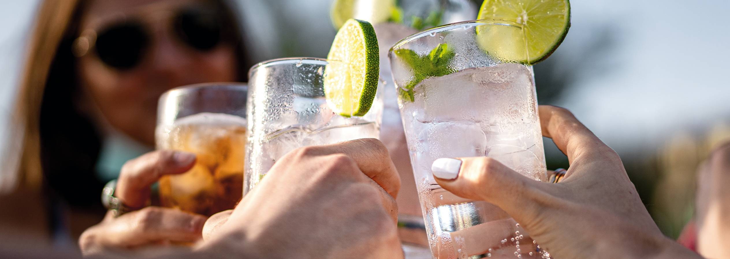 Venner skåler med kolde drinks med lime i solen.