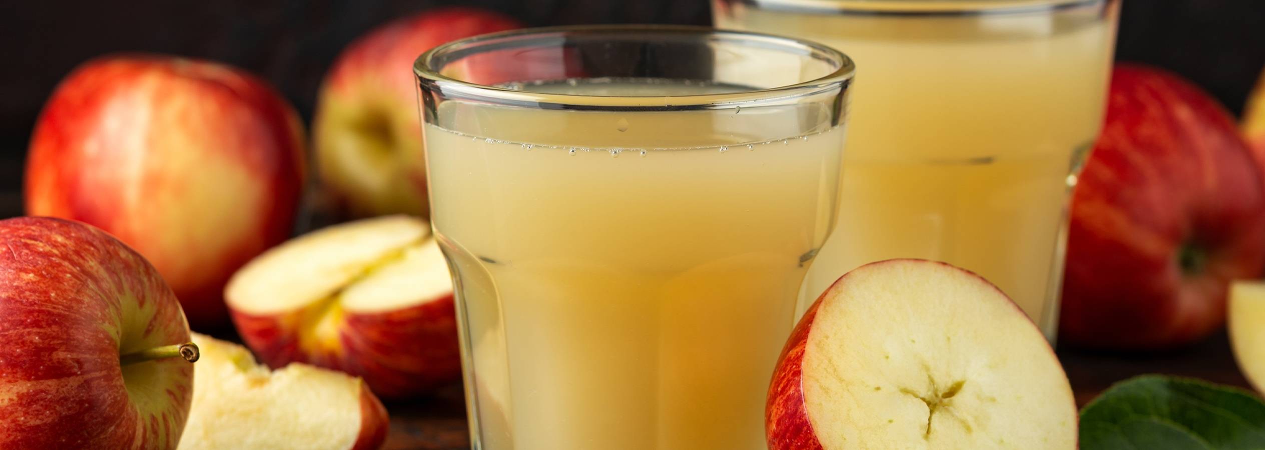 To glas æblejuice står foran et par røde æbler.