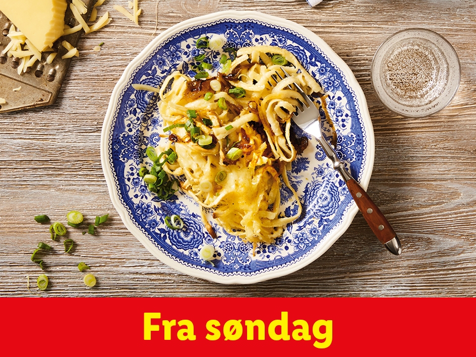 En tallerken med pasta og grøntsager, en gaffel, revet ost og et glas vand på et træbord.