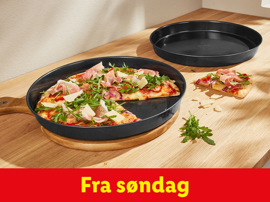 Pizza i en sort pande med en skive ved siden af på et træbord.