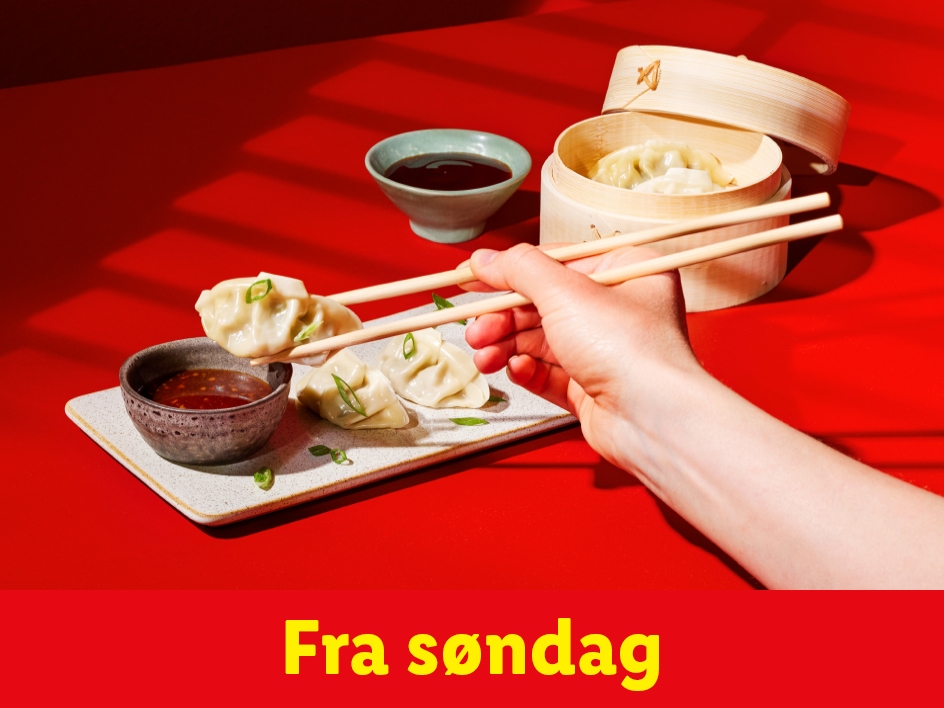 En hånd holder spisepinde med en dumpling over en skål med sauce, med flere dumplings på en tallerken og i en bambusdamper.