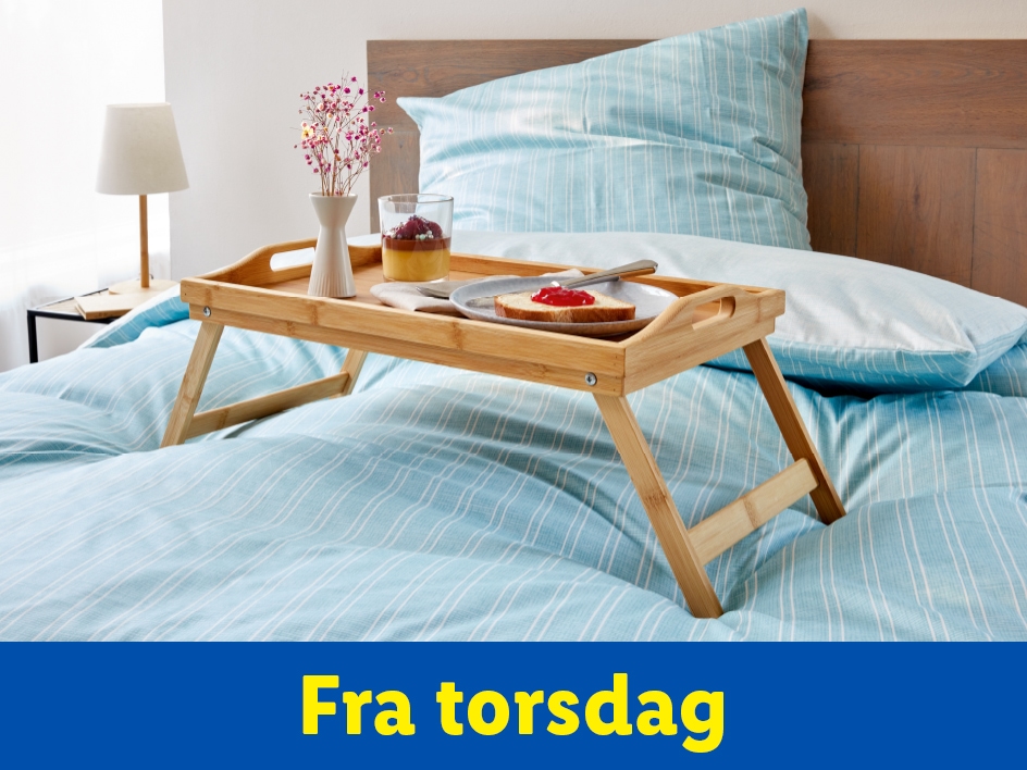 Morgenmad på sengen med en bambusbakke, en vase med blomster, en drink og en skive brød med syltetøj.