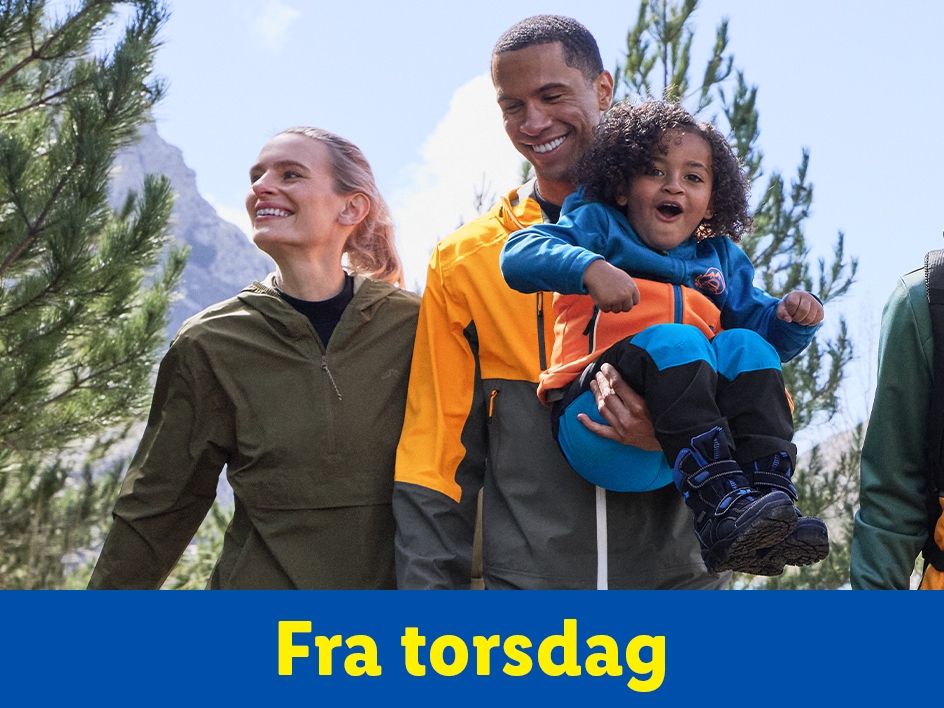 En familie i udendørstøj, hvor faren holder et barn, der griner, med bjerge i baggrunden.