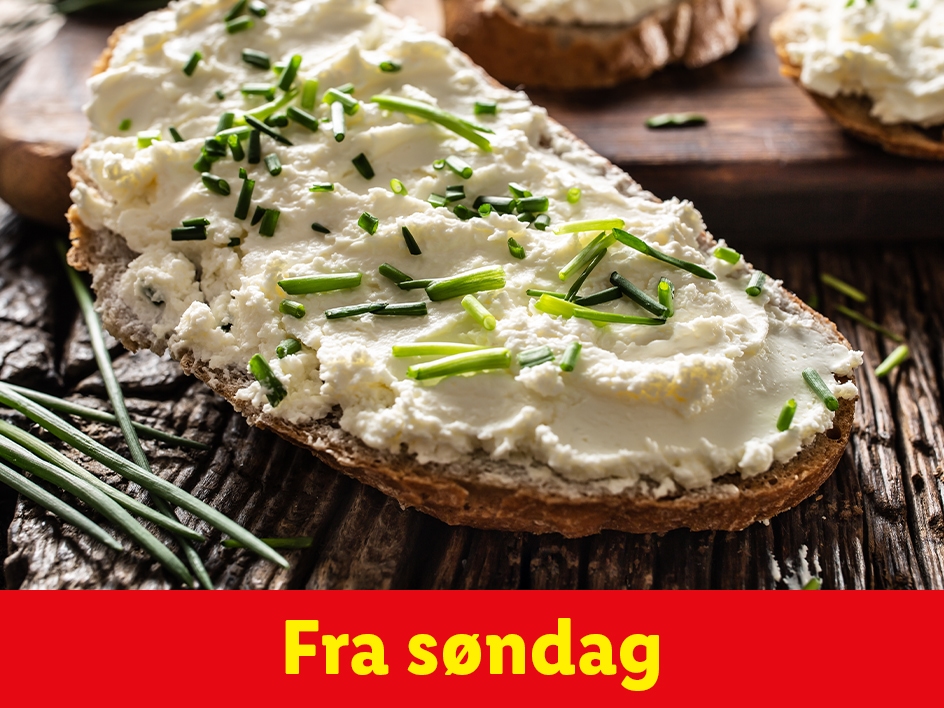 Brødskive med flødeost og purløg på et træbord.