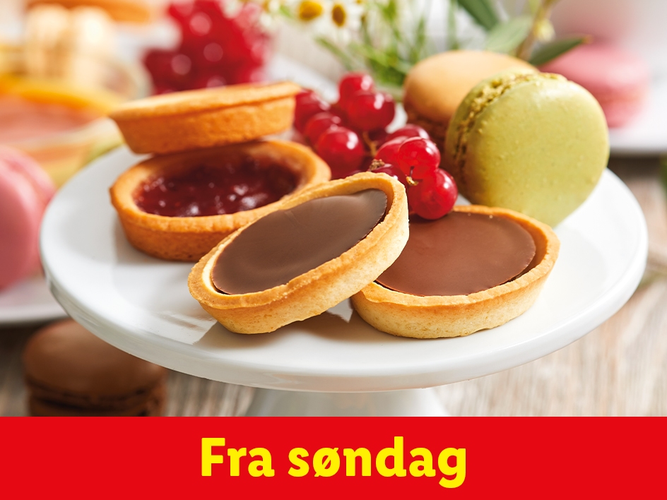 Et udvalg af tærter og makroner på et hvidt kagefad.
