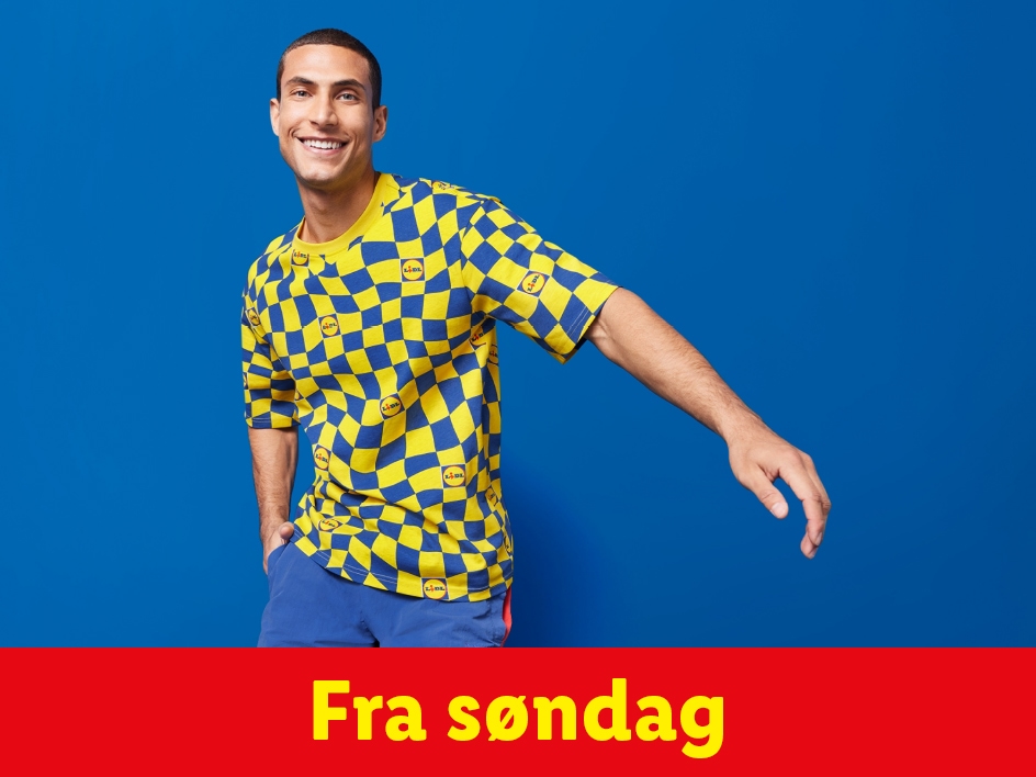 En mand i en gul og blå ternet T-shirt med Lidl-logoer og blå shorts, der smiler mod kameraet.