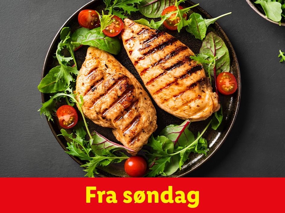Grillet kyllingebryst med salat og tomater på en sort tallerken.