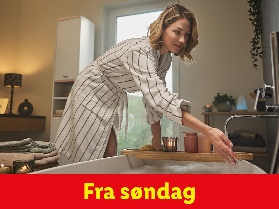 En kvinde i badekåbe fylder badekarret med varmt vand og skum.