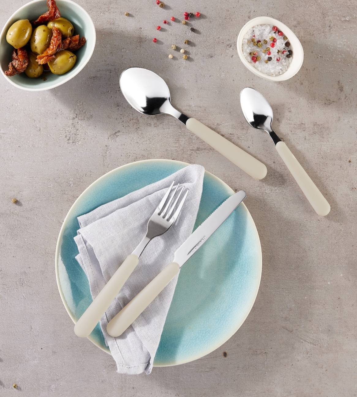 Bestiksæt med cremefarvede håndtag, inklusive gafler, knive og skeer, på et blåt fad.