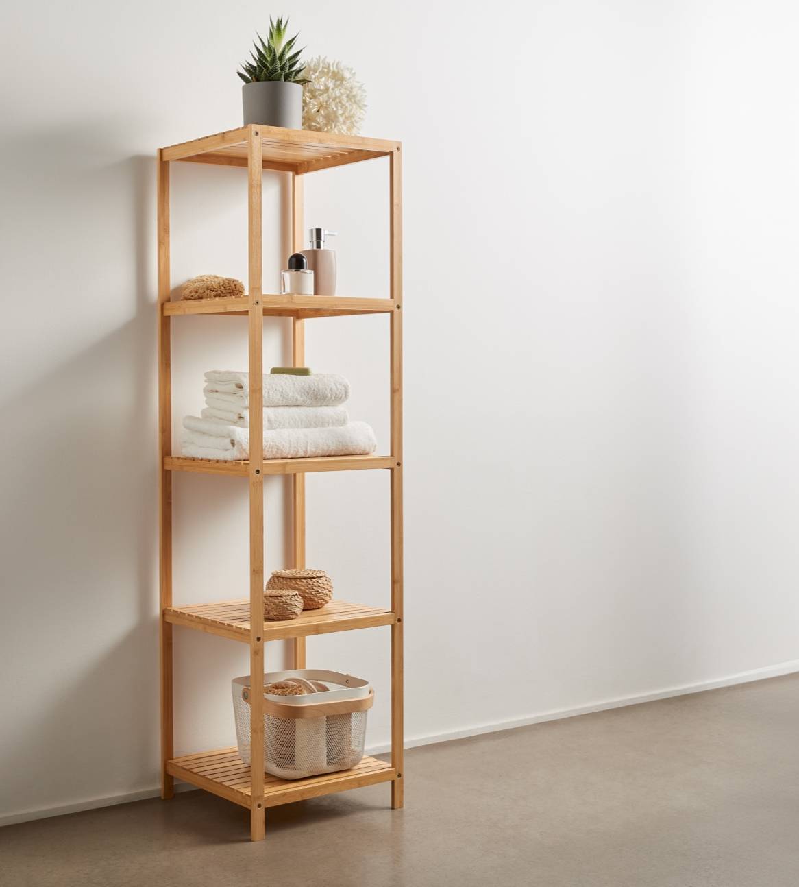 En bambus badeværelsesreol med håndklæder, toiletartikler og en plante.