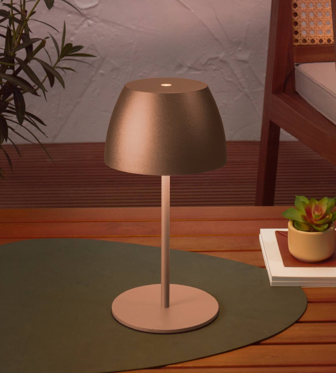 Bærbar bordlampe i bronze på et udendørs trædæk med planter.