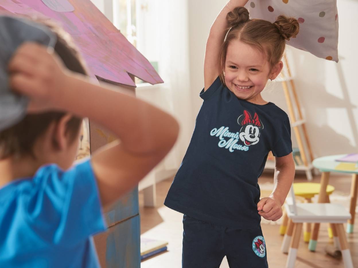 En pige i en Minnie Mouse t-shirt leger med en pude.
