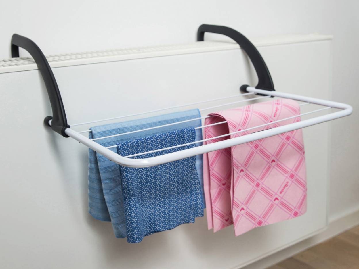 En hvid og sort tørrestativ hænger på en radiator og har håndklæder hængende.