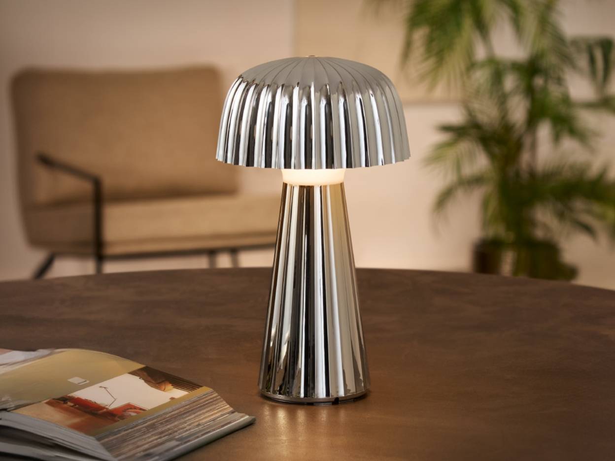 En moderne, sølvfarvet bordlampe med plisseret skærm på et træbord.
