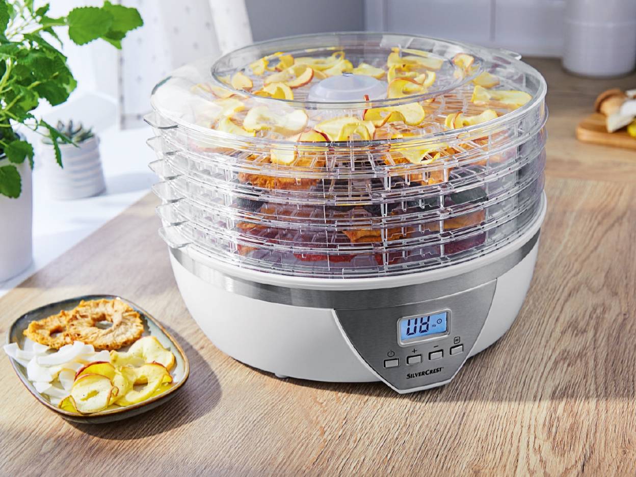 En SilverCrest fødevaredehydrator med flere etager fyldt med tørrede frugtskiver står på et træbord.