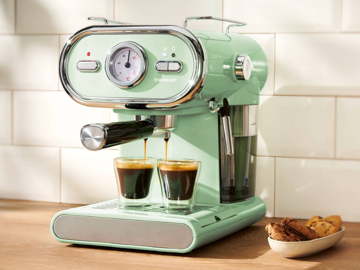 En mintgrøn SilverCrest espressomaskine brygger to kopper kaffe på en træbordplade.