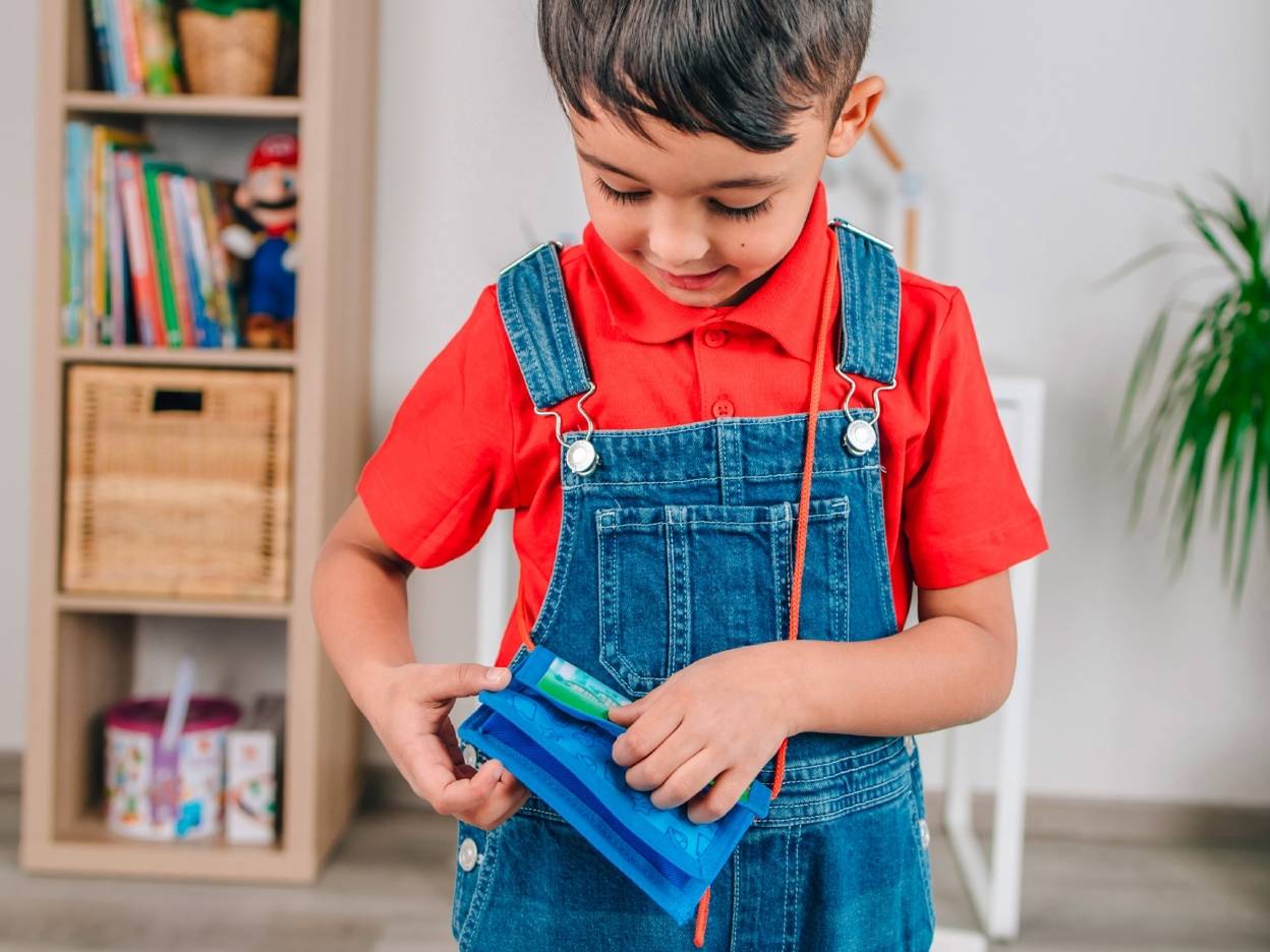 En lille dreng i rødt tøj og denim overalls leger med en blå pung.