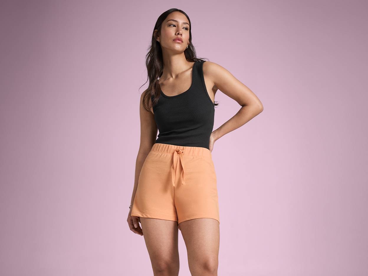 En model iført en sort tanktop og orange shorts.
