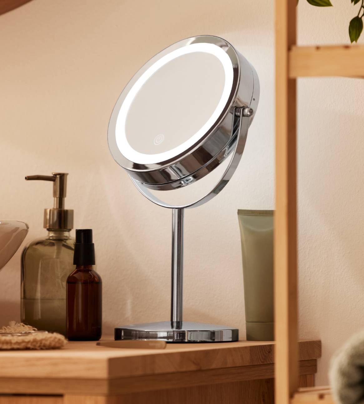 Et elegant, kromspejl med LED-lys står på et badeværelsesbord med forskellige toiletartikler.