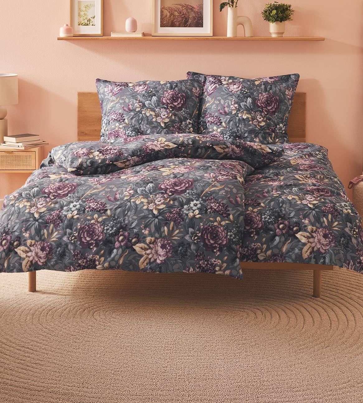 Et mørkegråt sengetøj med blomsterprint på en seng med træben.