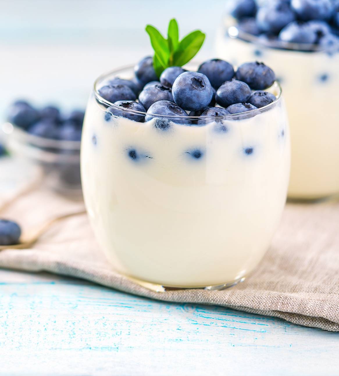 Yoghurt med blåbær i glas på et lyst træbord.