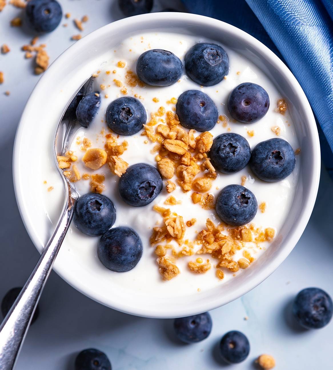 En hvid skål med yoghurt, blåbær og granola med en ske i.