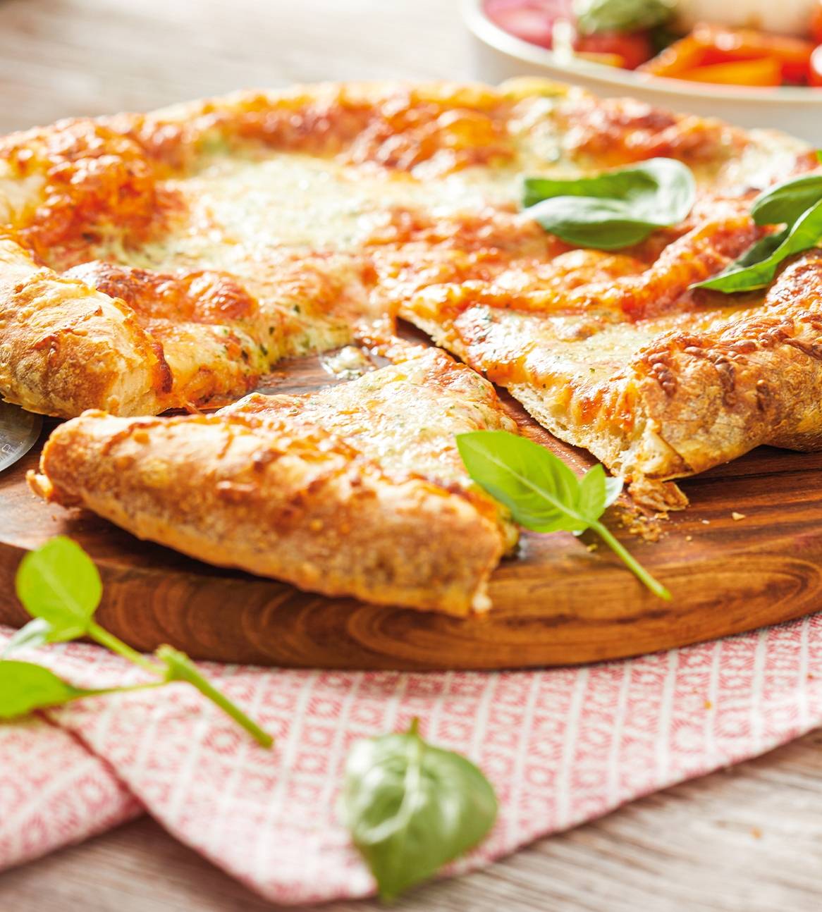 En lækker pizza med ost og basilikum serveret på en træplade.