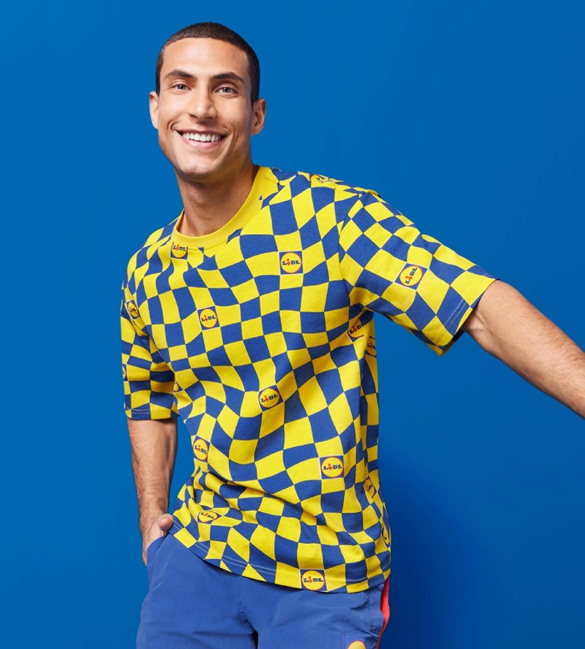En smilende mand i en gul og blå ternet Lidl T-shirt og blå shorts.