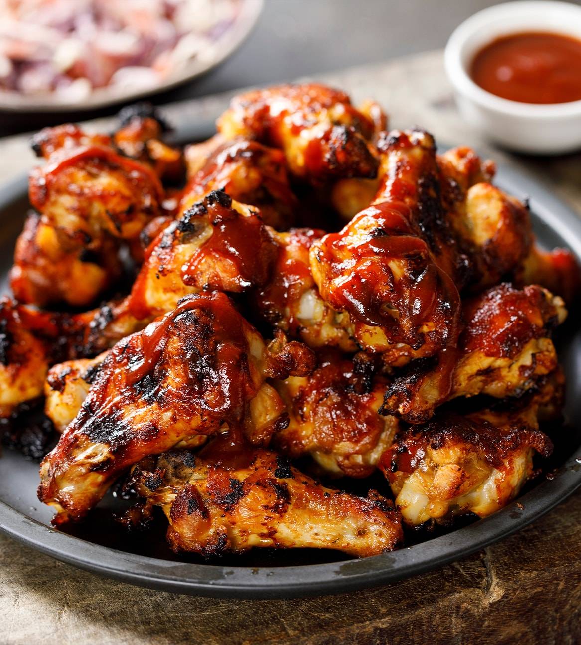 En skål med lækre, grillede kyllingevinger overdækket med BBQ-sauce.