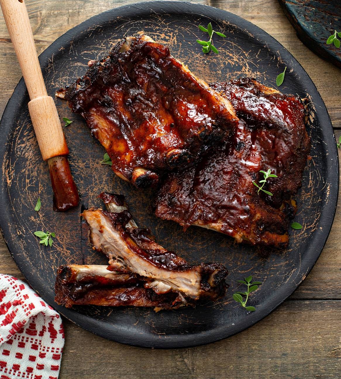 BBQ-ribben serveret på en mørk tallerken med en pensel med BBQ-sauce.