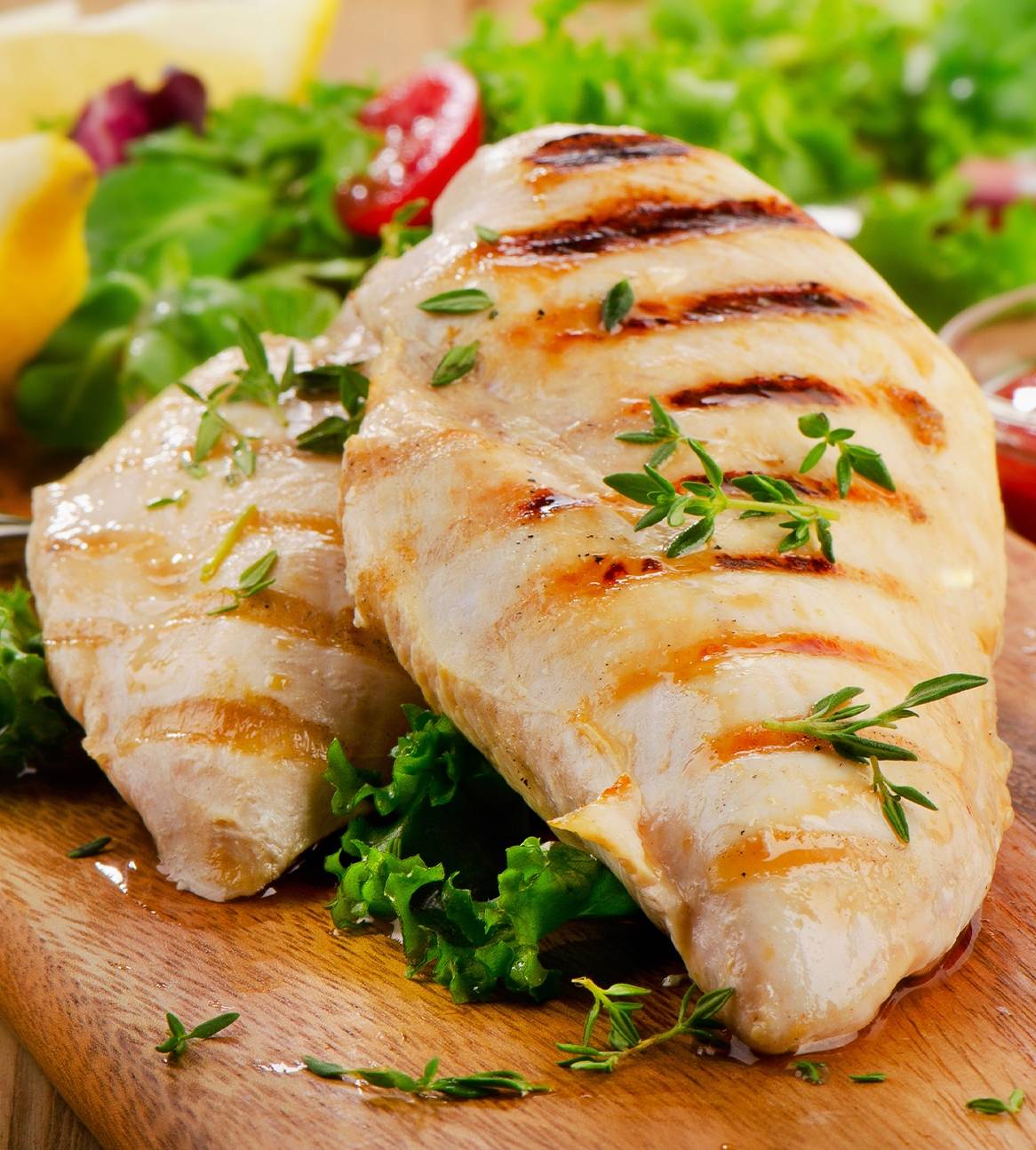 Grillet kyllingebryst med salat og citron på et træskærebræt.