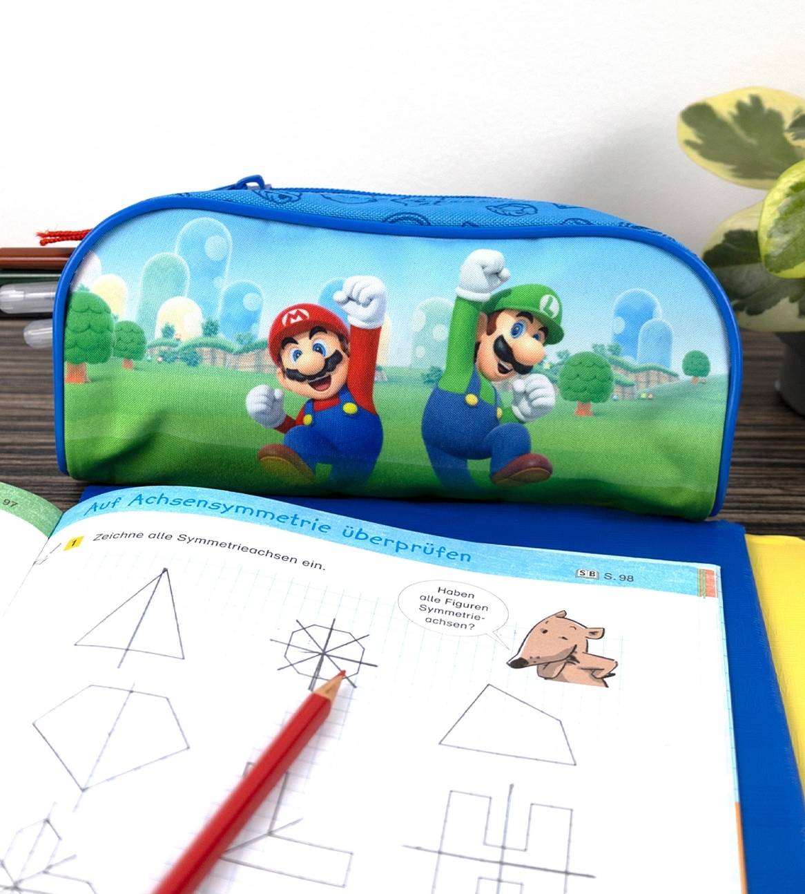 En blå Super Mario penalhus ligger oven på en matematikopgavebog.