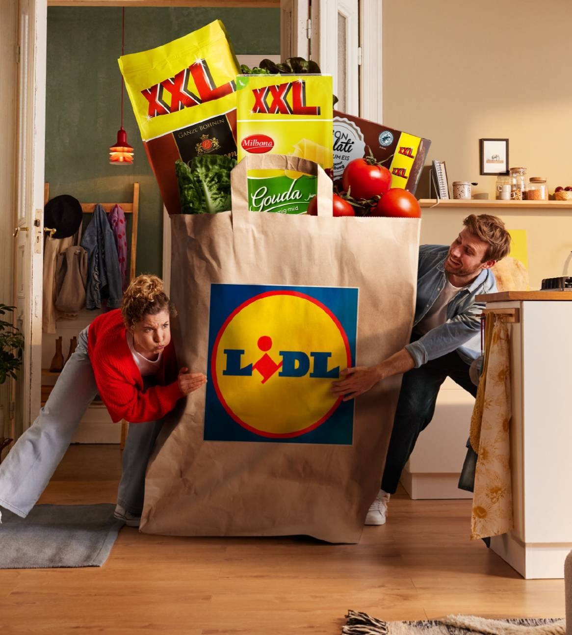 Et par skubber en overdimensioneret Lidl-indkøbspose fyldt med XXL-produkter.
