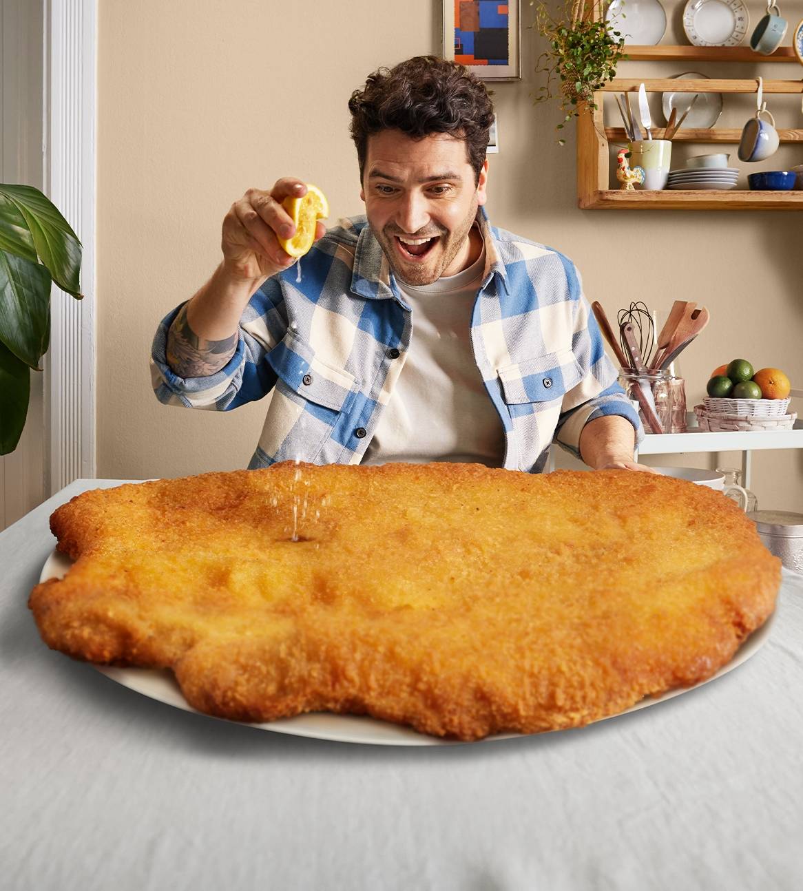 En mand drysser citronsaft over en kæmpe schnitzel på en tallerken.