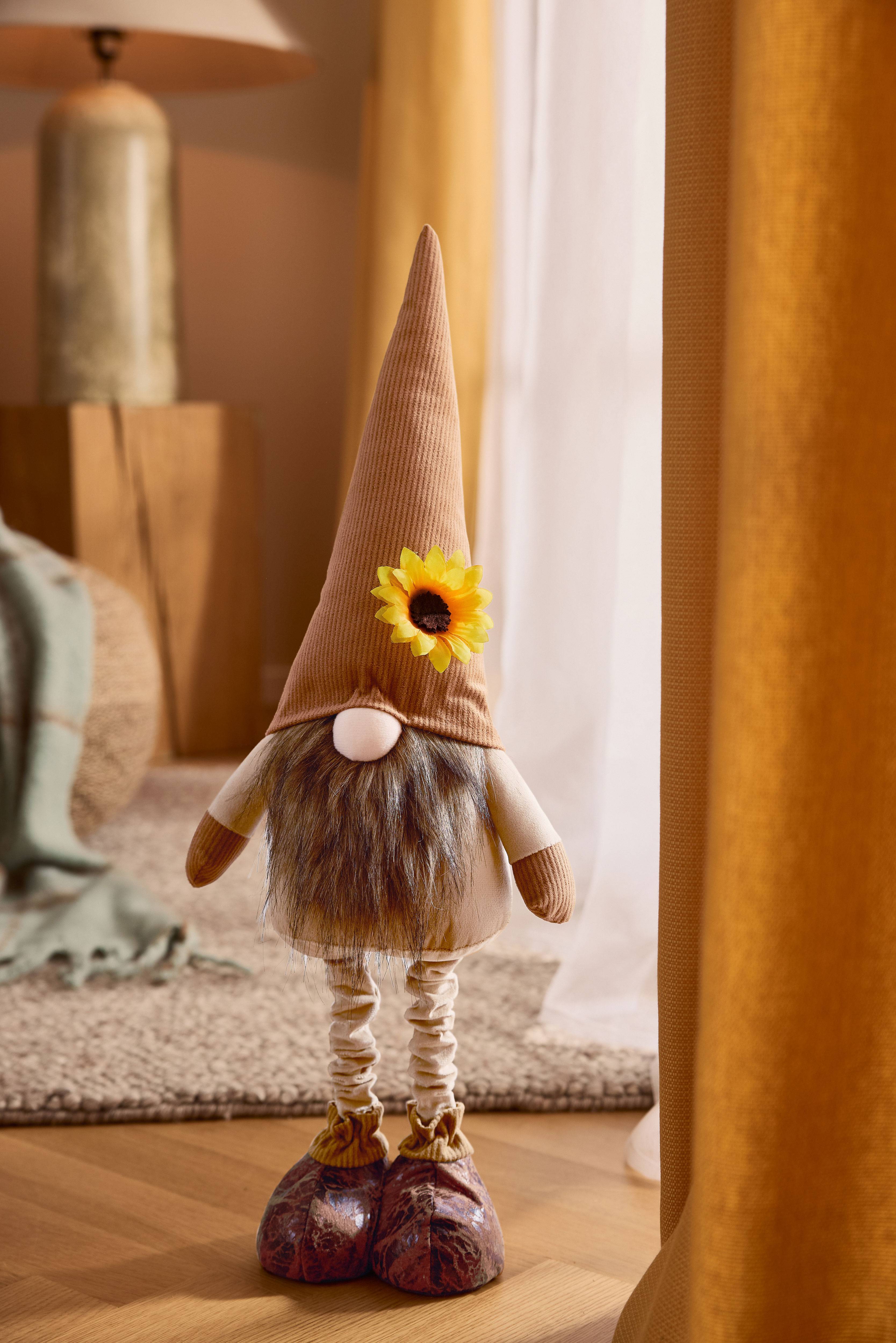 Plys-nisse med brun spids hat, skæg og solsikke, i hyggelige omgivelser.