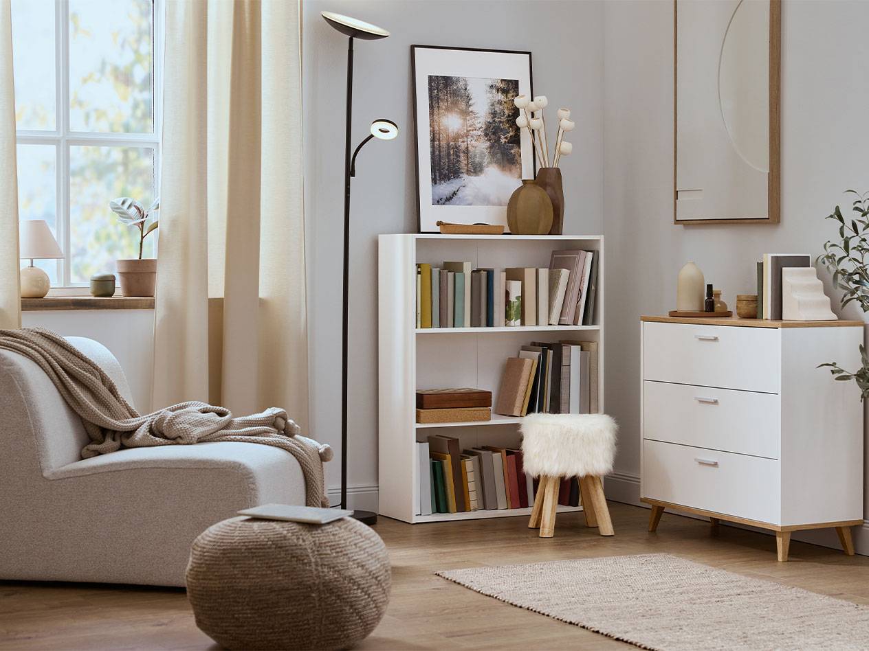 Hyggelig stue med lænestol, bogreol og kommode i neutrale farver.