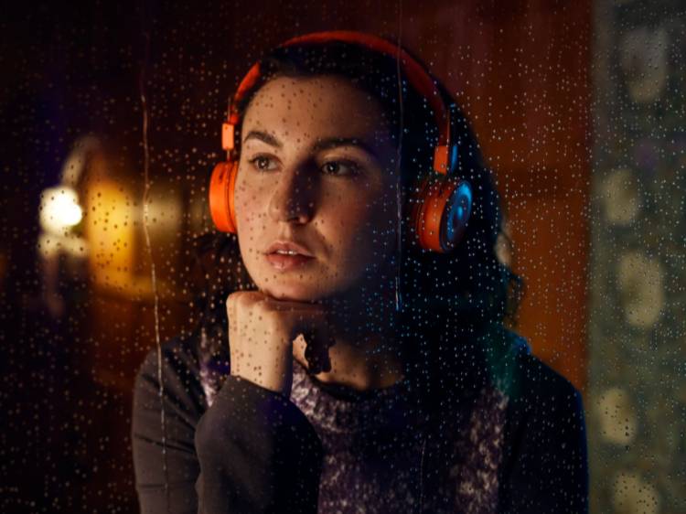 Kvinde med orange hovedtelefoner kigger ud af et regnvådt vindue.