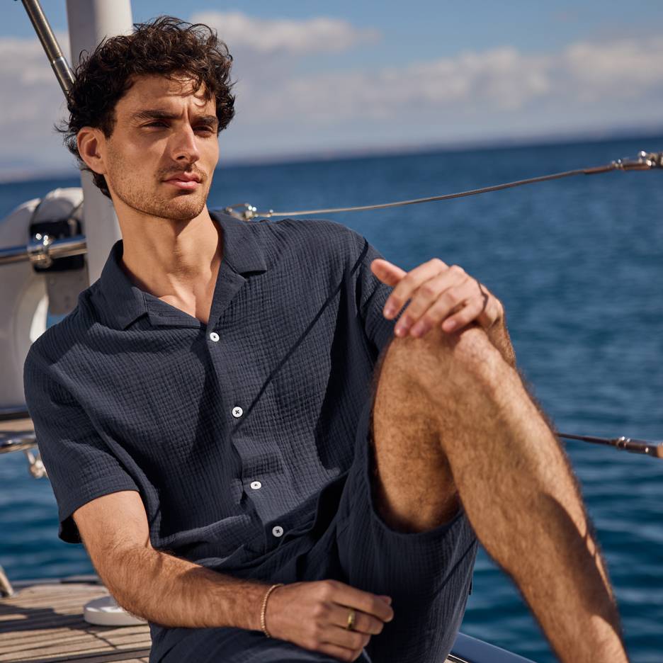 Mand i mørkeblå skjorte og shorts på en yacht, der kigger ud over havet.