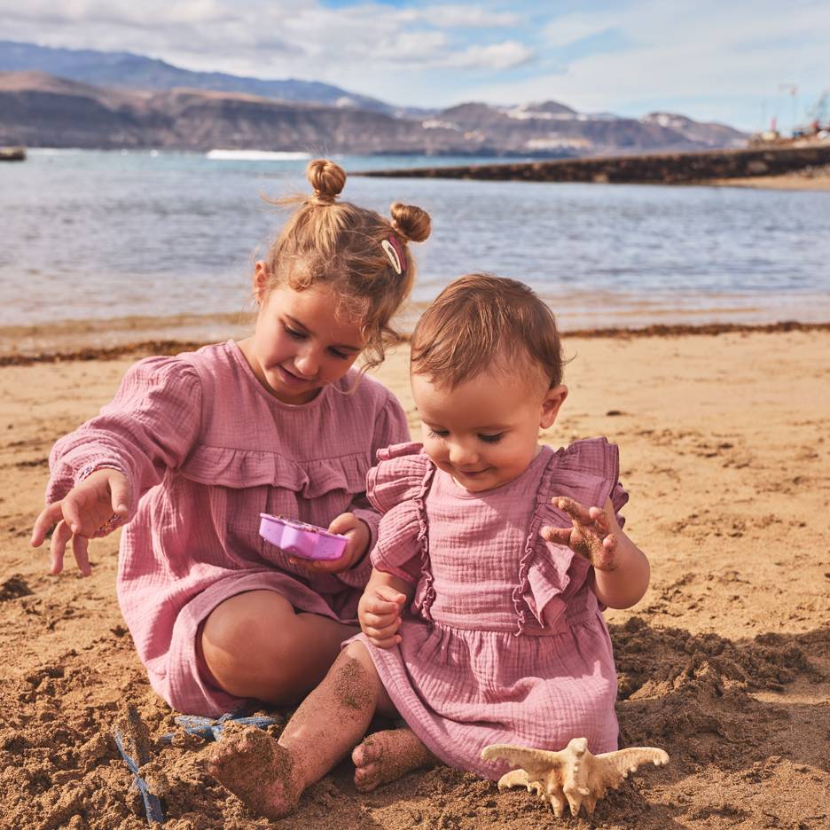 To piger i lyserøde kjoler leger i sandet på stranden.