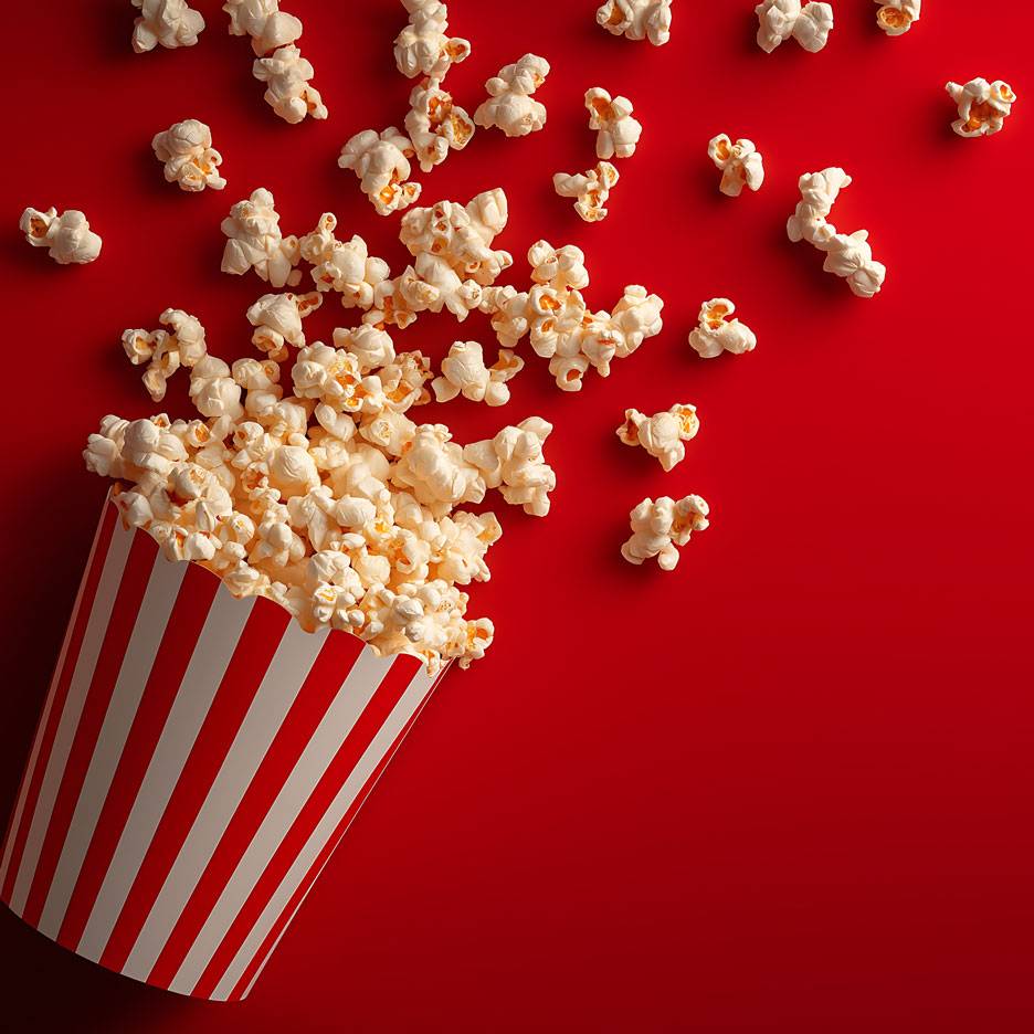 Popcorn på rød baggrund, en del af popcornene i en stribet papkop.