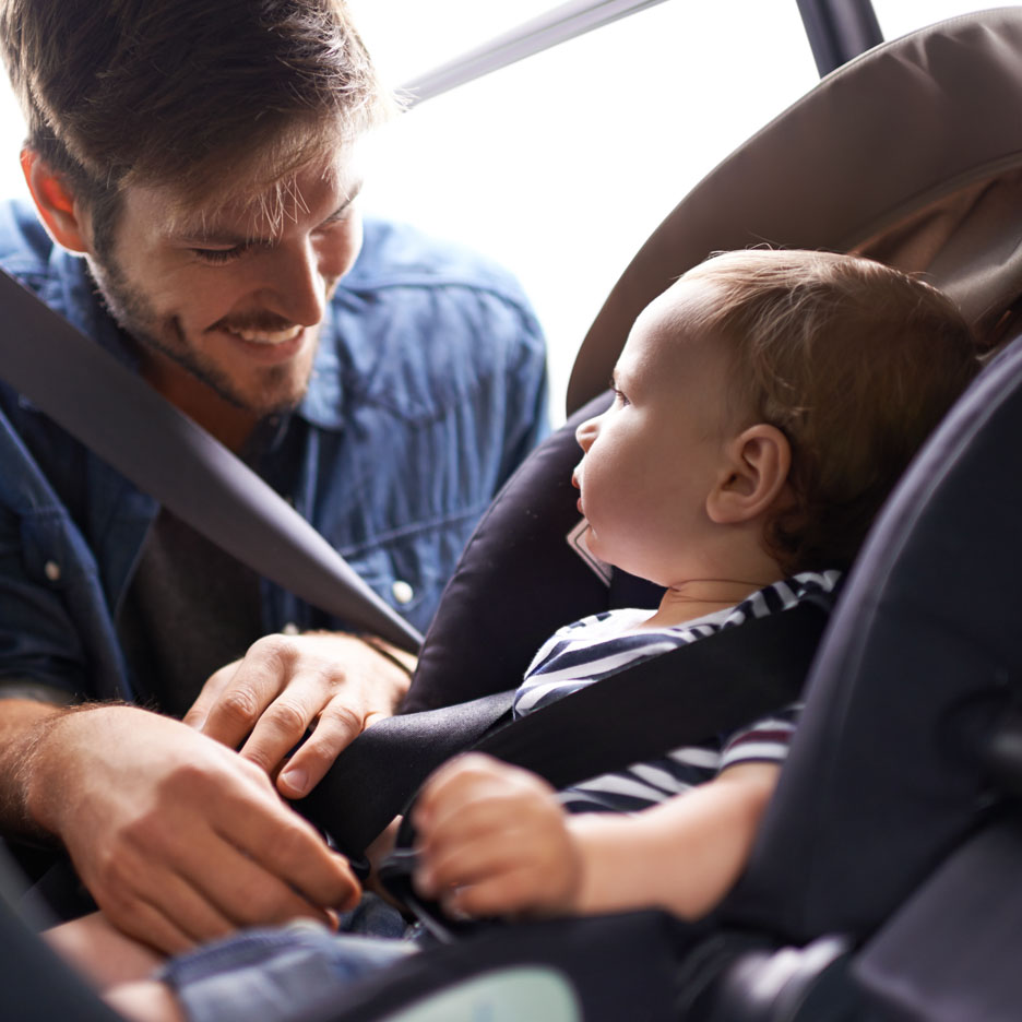 En far spænder sin baby fast i en autostol.