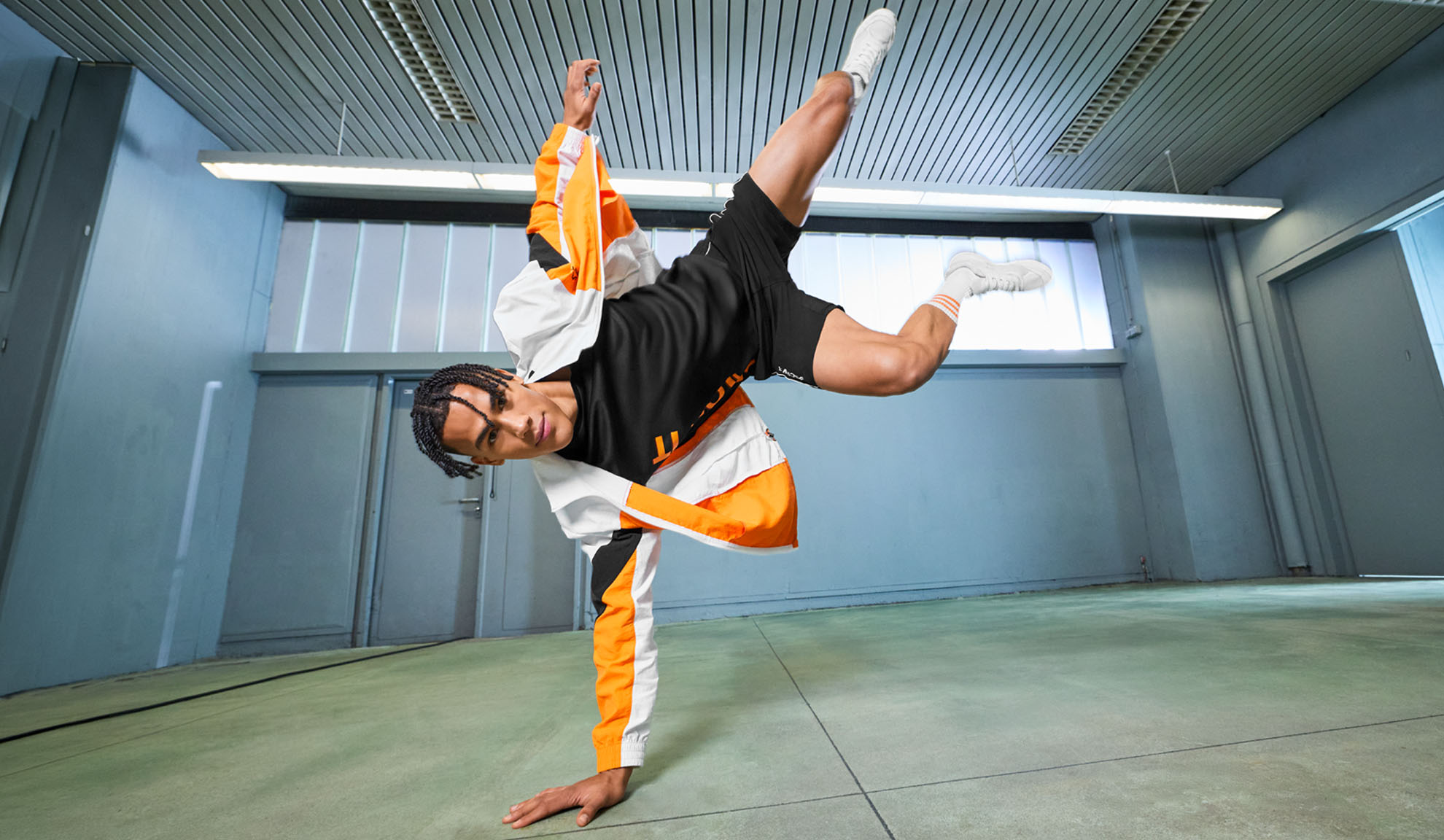 Mand i sportstøj, sort t-shirt, shorts og orange og hvid jakke, udfører et dansetrin.